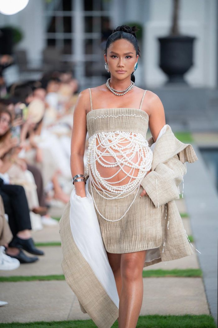  Người đẹp diện thiết kế hai mảnh, kết hợp giữa áo crop-top và chân váy. Bụng bầu của cô được che bằng những chiếc dây ngọc trai. Khác với những lần catwalk trước đây, H'Hen Niê chọn giày cao gót có chiều cao vừa phải để thoải mái khi di chuyển và đảm bảo an toàn. Màn catwalk của H'Hen Niê gây chú ý trên mạng xã hội. Cô nhận nhiều lời khen vì vẫn giữ được thần thái và bước đi chuyên nghiệp trên sàn diễn dù bụng bầu khá to. 